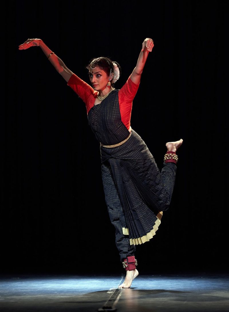 Arms raised, one leg lifted, in black and red